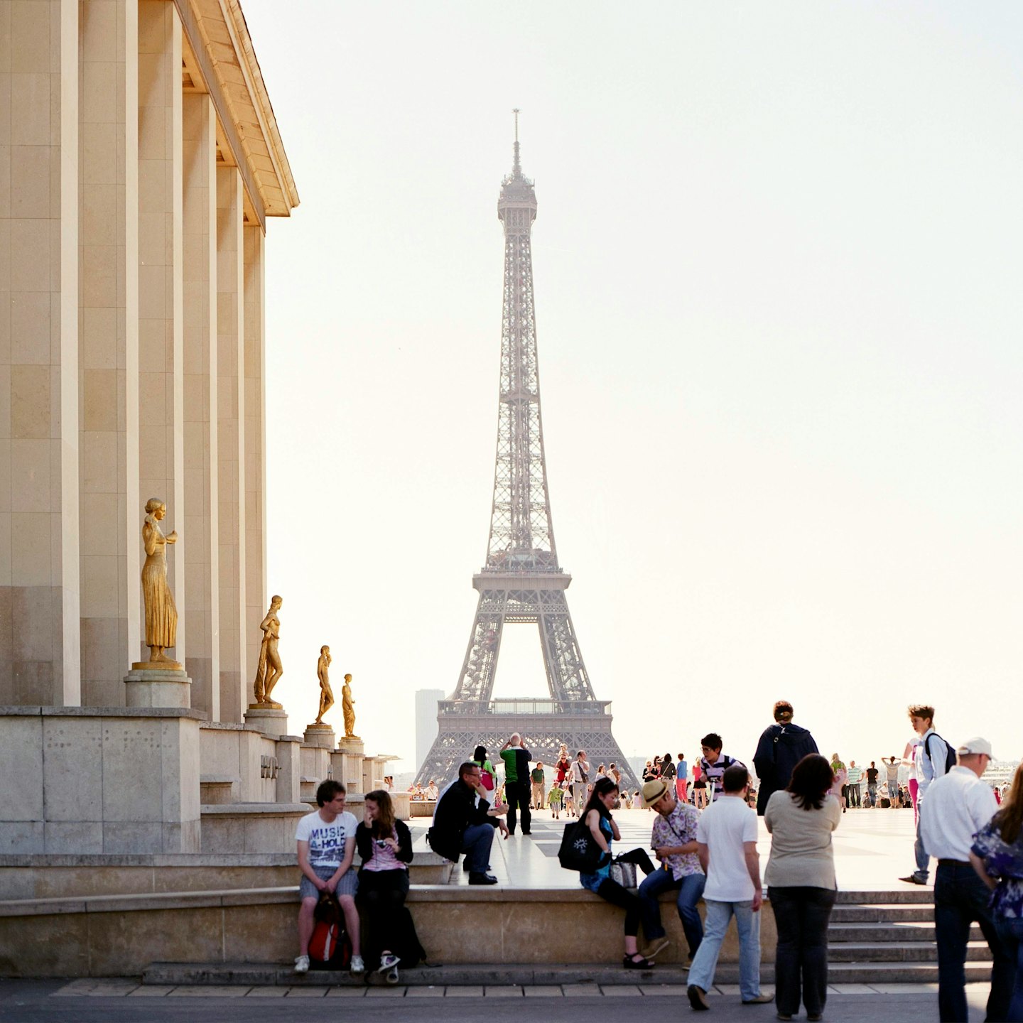 People relaxing on stone terraces near statues with the Eiffel Tower in the distance.