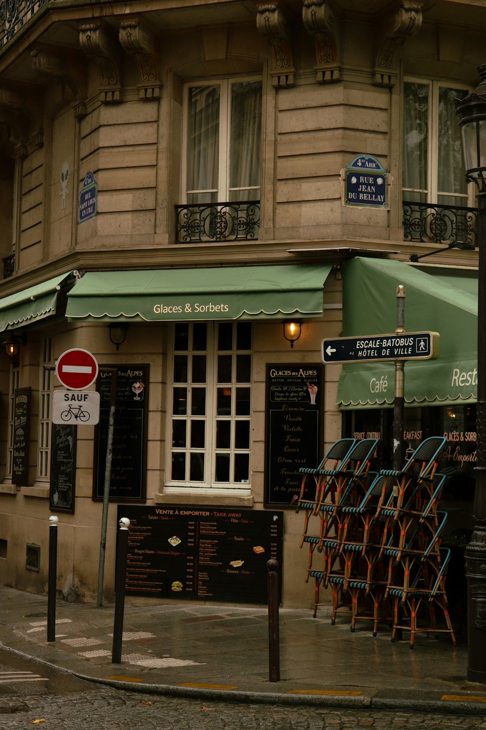 Parisian cafe corner with green awnings and stacked outdoor chairs.