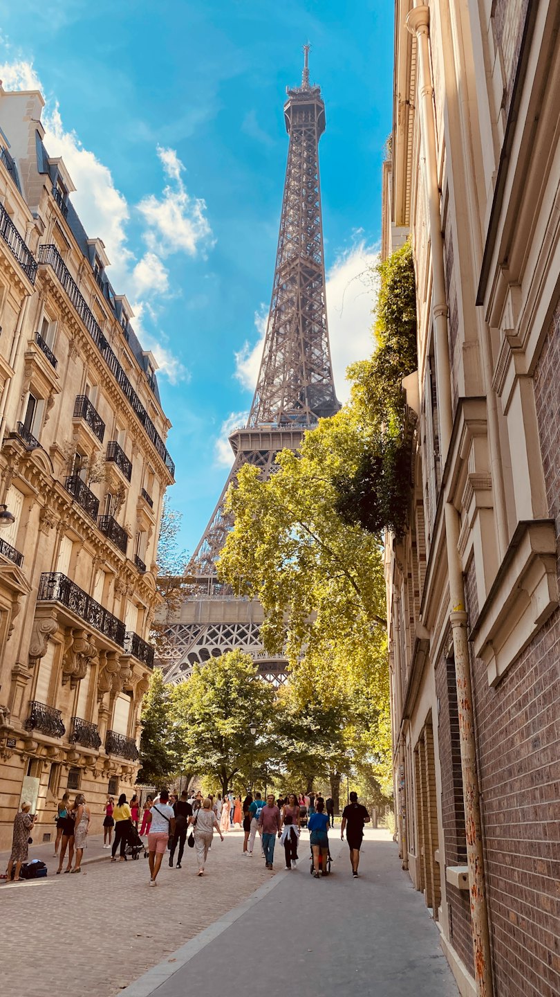 People walk along a Parisian street with the Eiffel Tower.